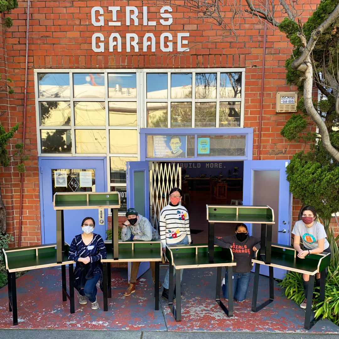 Girls display distance learning desks in front of Girls Garage